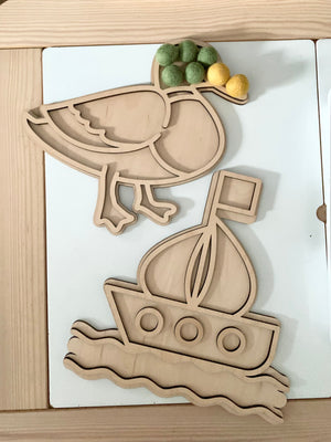 Fillable duck-shaped play tray with green and yellow felt balls and wooden sailboat tray on white surface