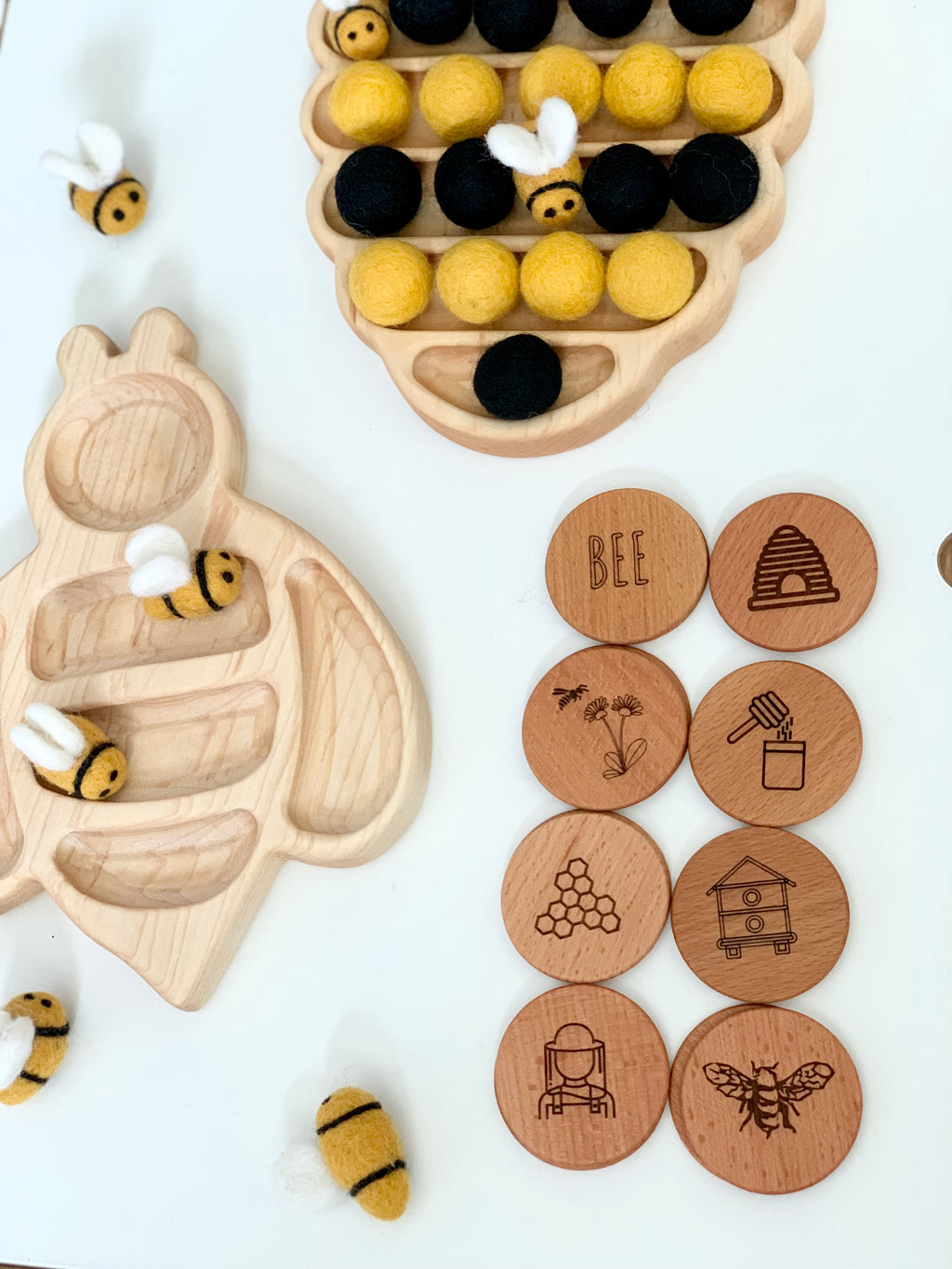Bee themed memory game with wooden tokens engraved with bee illustrations and felt bee playing pieces on white background