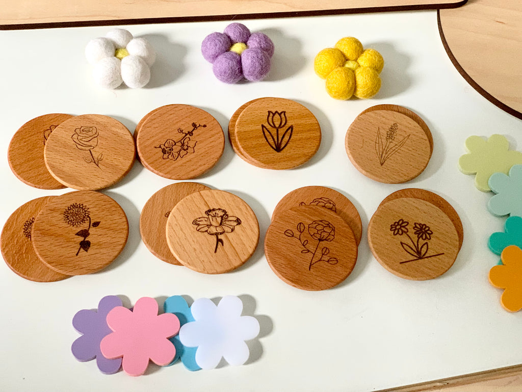 Round wooden memory game coins engraved with flower illustrations and colorful flower-shaped pieces on white surface