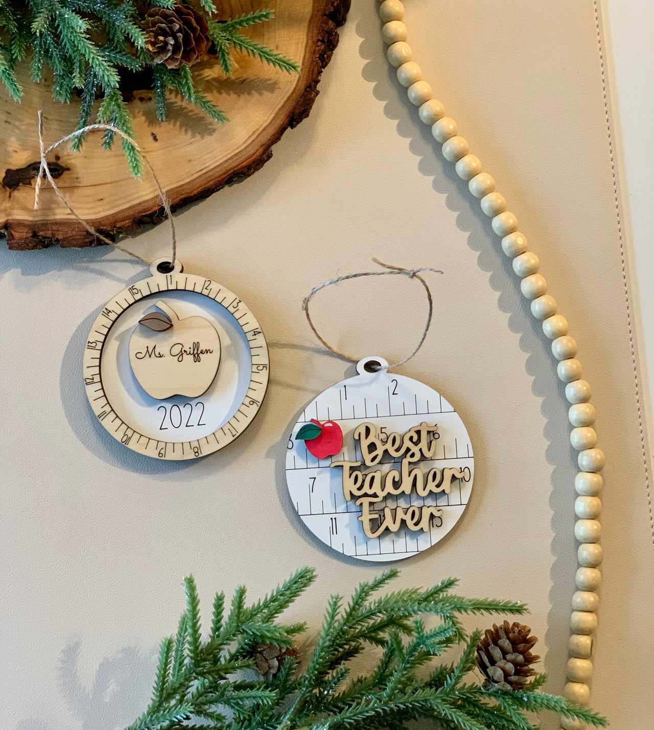 Two round wooden teacher Christmas ornaments with engraved apple and "Best teacher ever" text on light background
