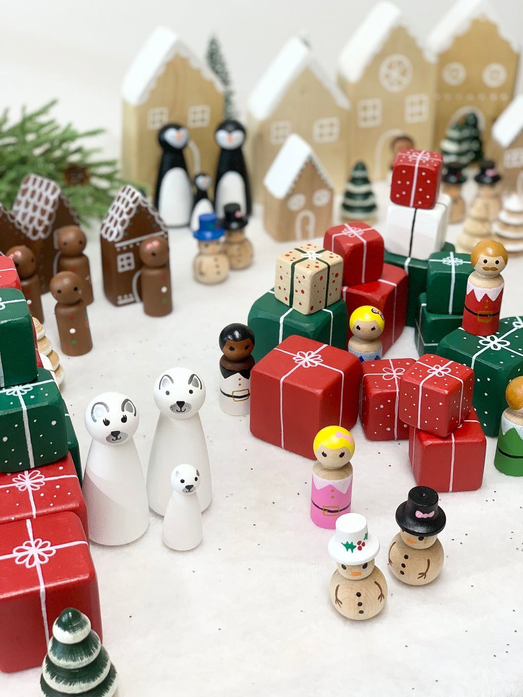 Hand-painted wooden polar bear and penguin family figurines surrounded by stacked wrapped gift boxes on white surface