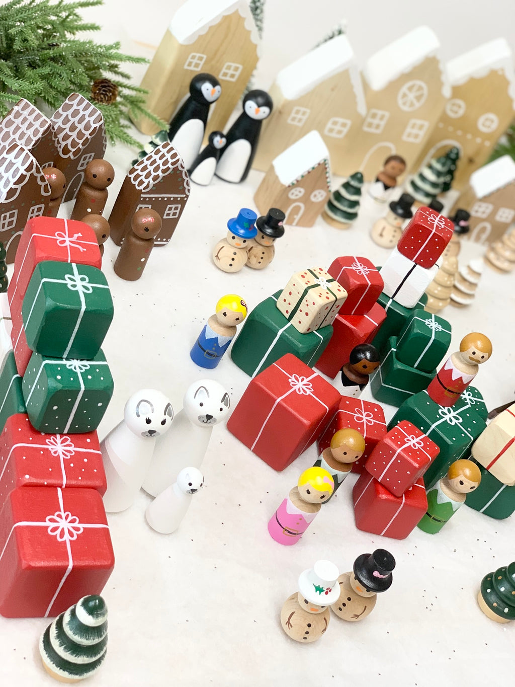Hand painted wooden holiday village scene with stacked red and green gift boxes and small figurines on white surface