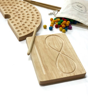 Light natural maple wooden infinity figure eight tracing board with stylus surrounded by colorful felt balls and wooden pegboard on white background