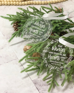 Clear round acrylic memorial Christmas ornaments engraved with white script and floral design, resting on pine branches