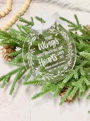 Clear round acrylic memorial Christmas ornament with white engraved wreath and personalized text on greenery background