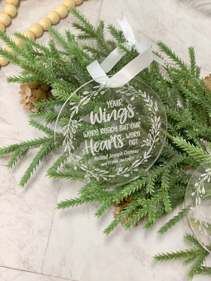 Round clear acrylic memorial Christmas ornament with white engraved script and leaf wreath design on greenery background