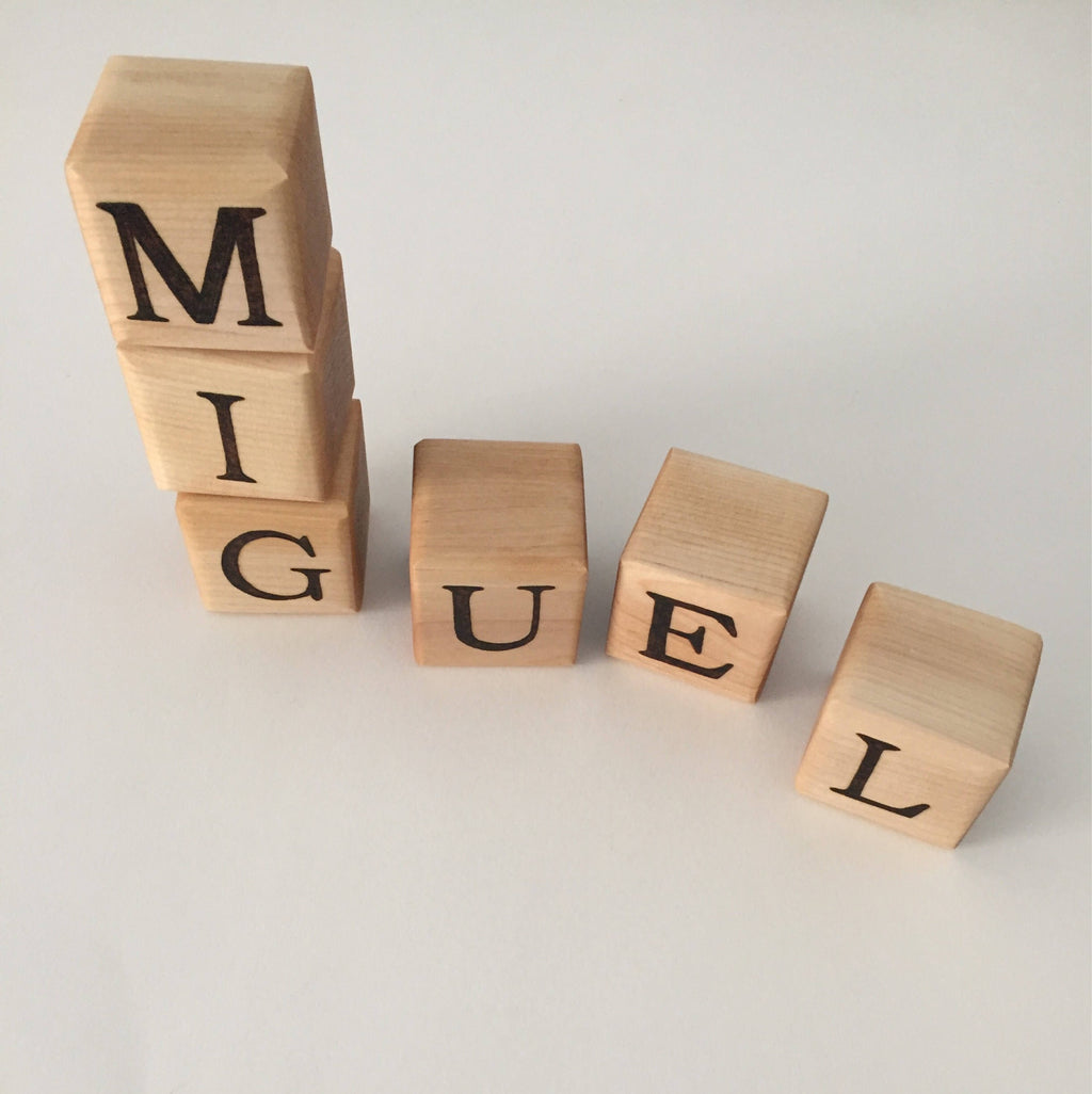 Natural wooden 1.5 inch alphabet blocks with black letters spelling MIGUEL on white background