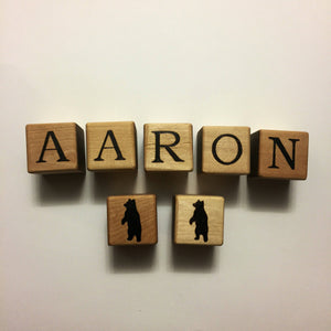 Natural wooden 1.5 inch alphabet blocks spelling AARON with two blocks featuring black bear silhouettes on white background