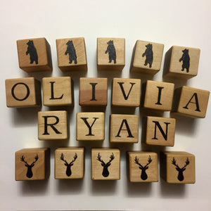 Natural wooden 1.5 inch alphabet blocks with black letters spelling OLIVIA RYAN and bear and deer silhouettes on white background