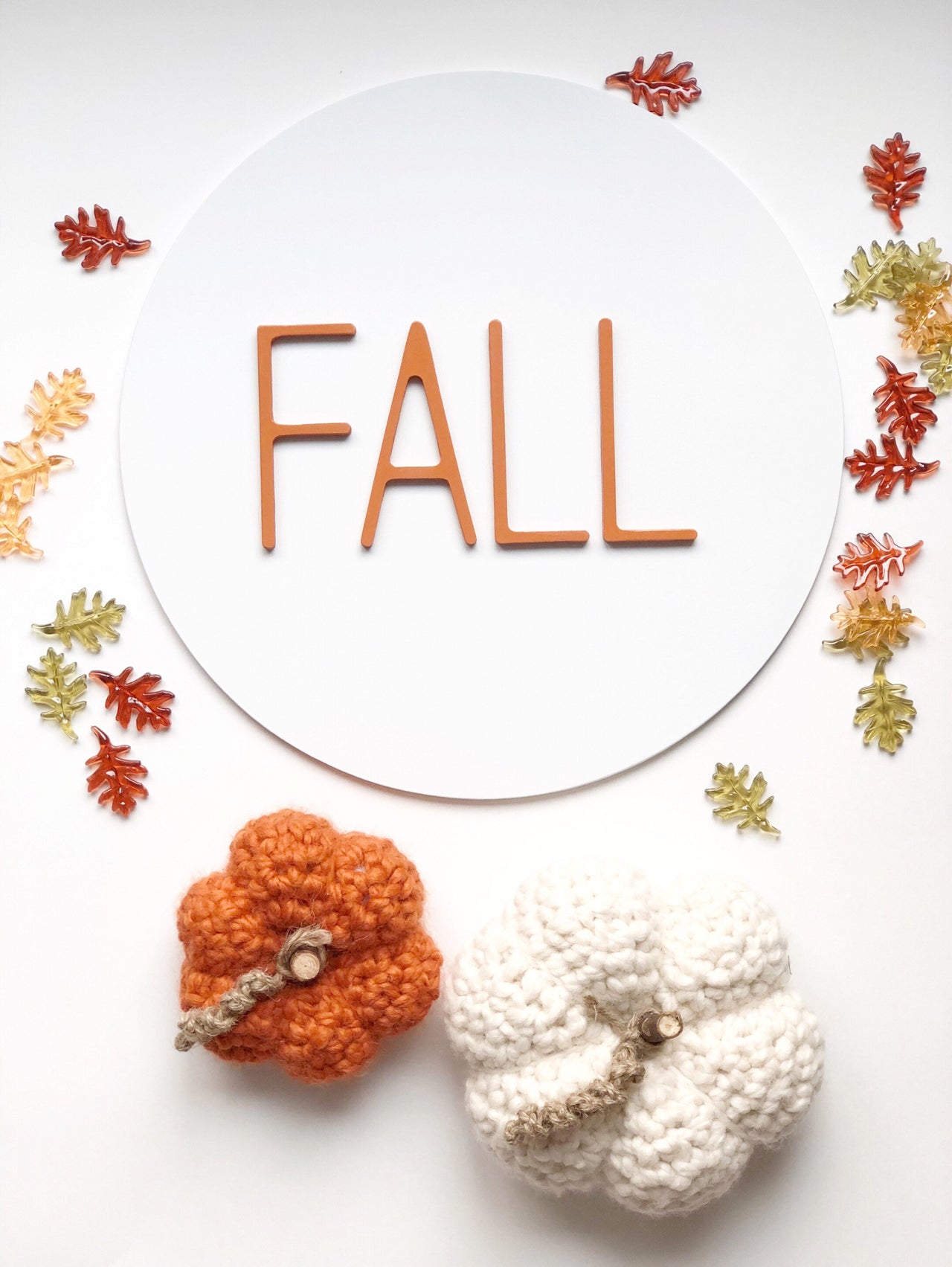 3D fall sign made from layered MDF surrounded by colorful decorative leaves and knitted pumpkins.