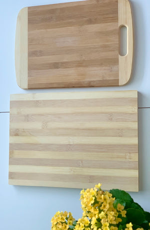 Two natural bamboo cutting and serving boards with striped patterns and a yellow flowering plant on white surface