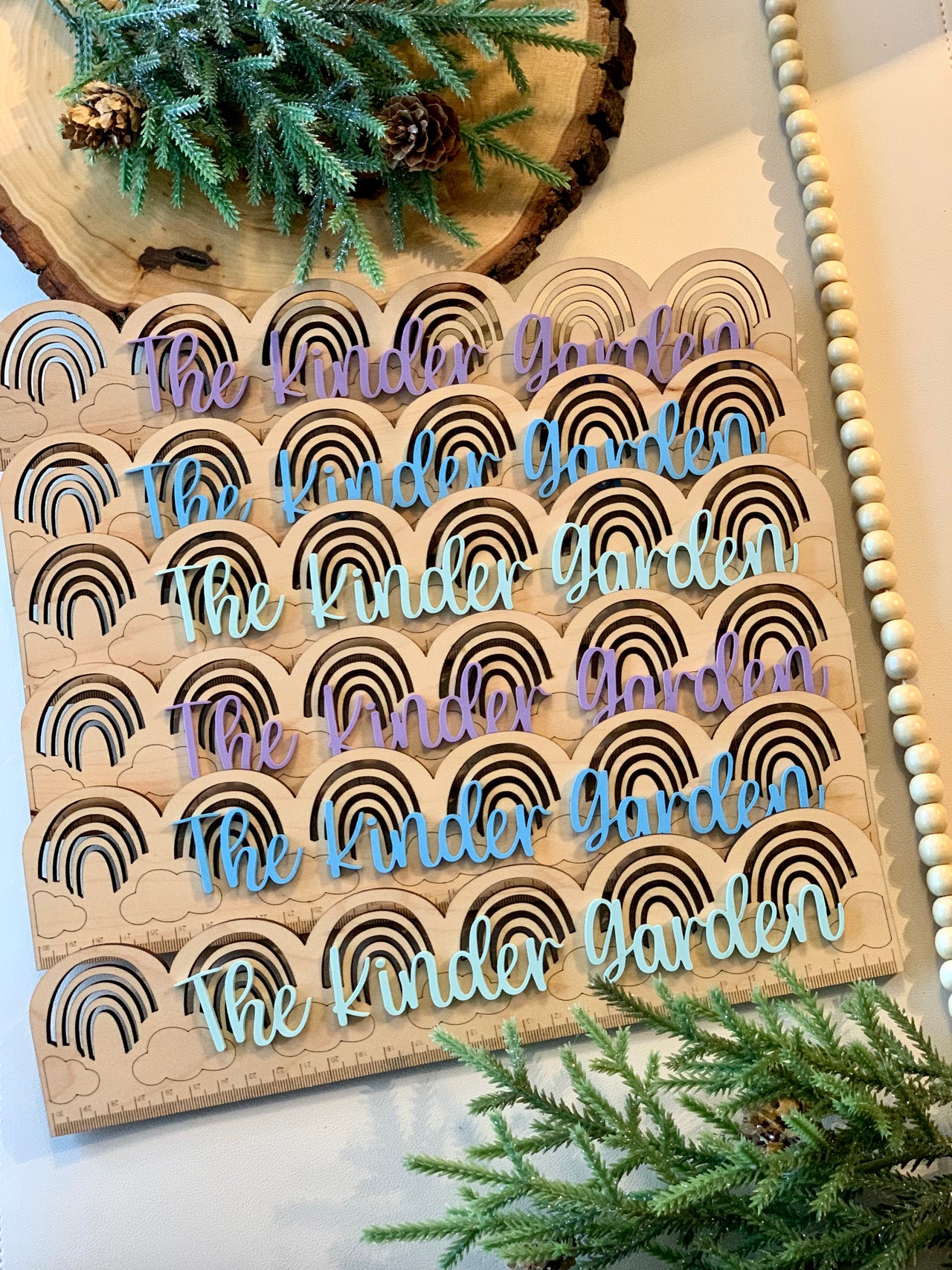 Personalized wooden rainbow rulers with engraved black rainbows and handwritten style text in pastel colors on natural wood background