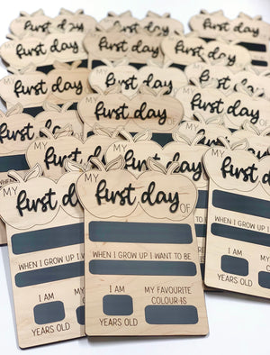Multiple wooden reversible chalkboard signs shaped like apples with "first day" text and fill-in fields stacked together