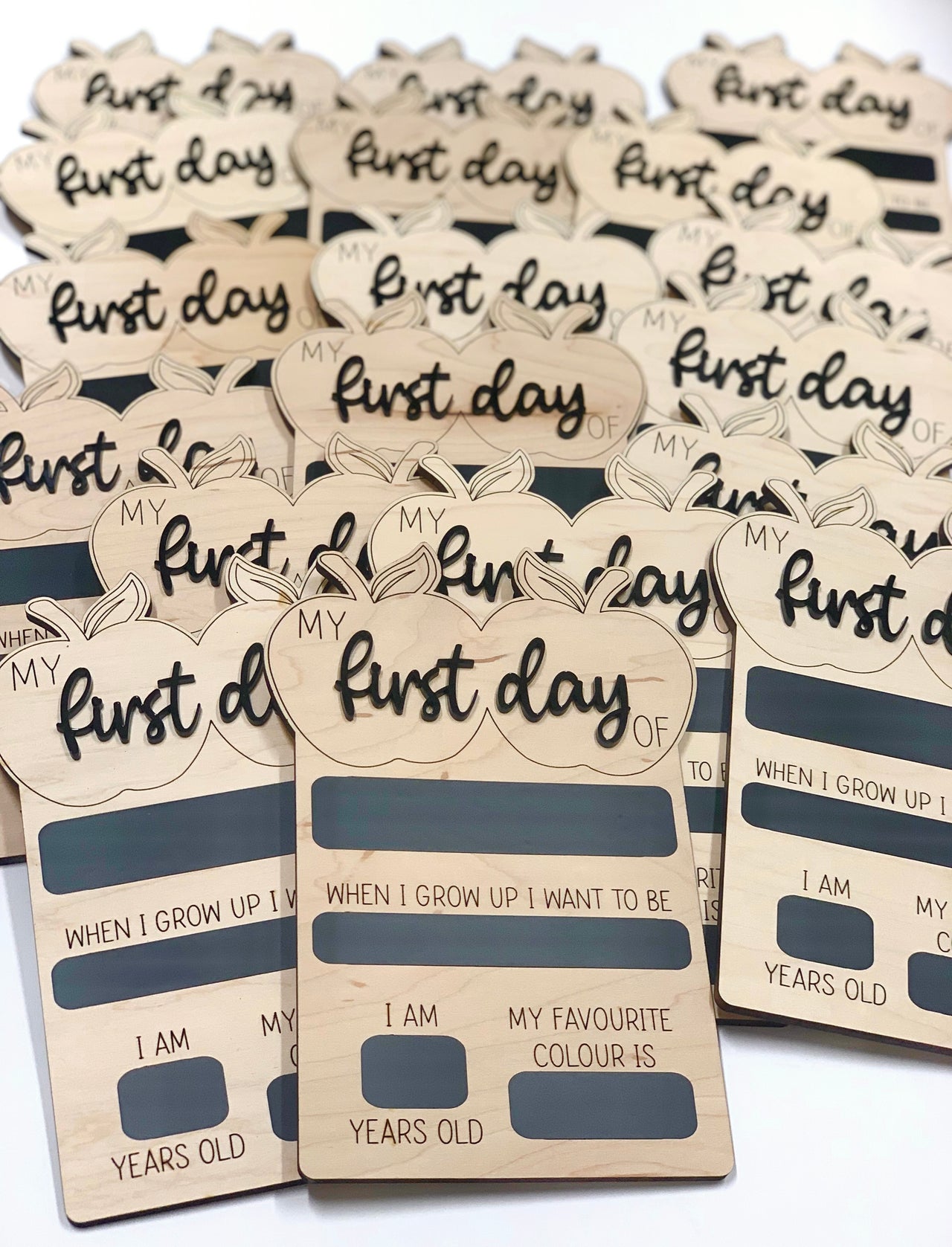 Multiple wooden reversible chalkboard signs shaped like apples with "first day" text and fill-in fields stacked together