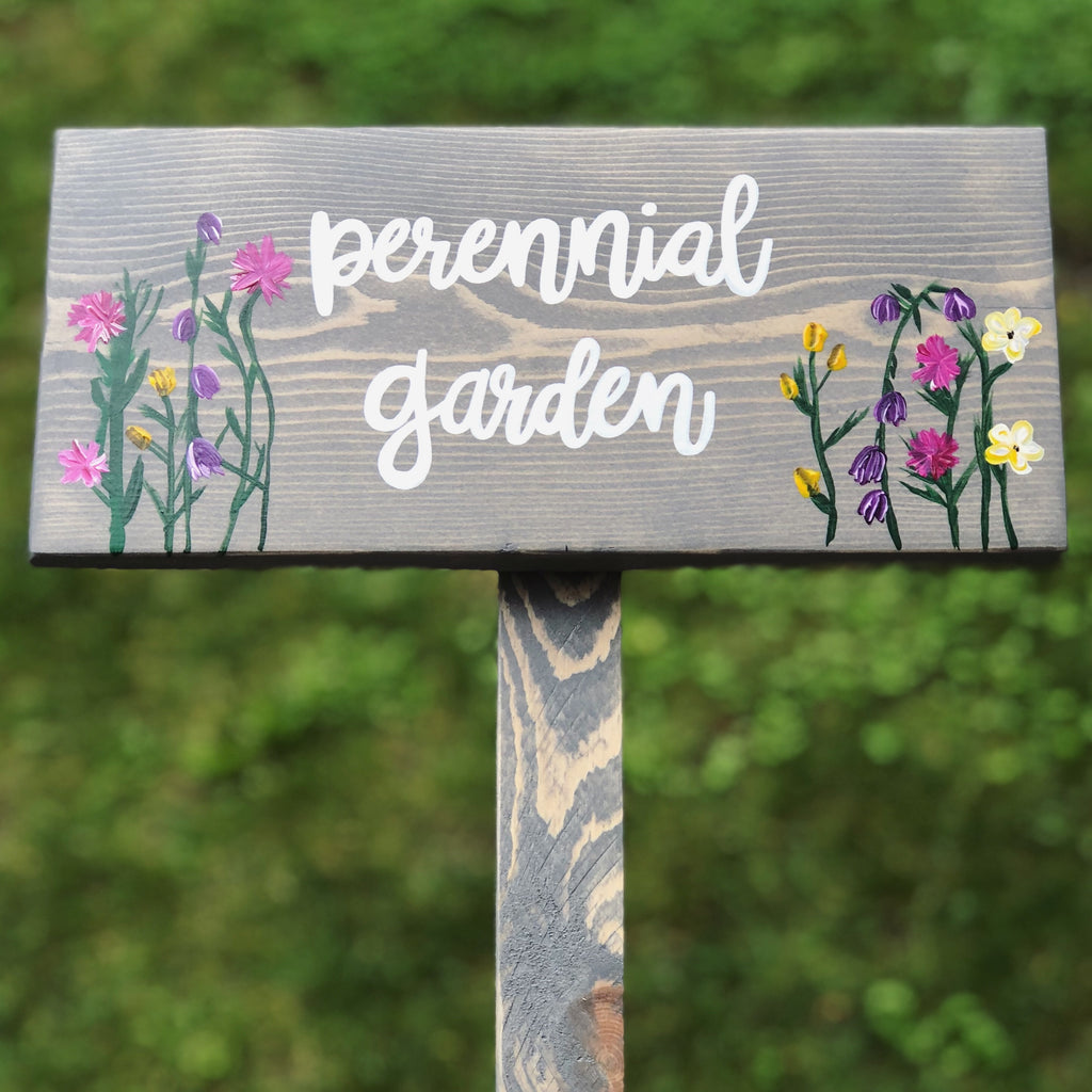 Large custom wooden garden sign painted gray with white cursive "perennial garden" letters and colorful floral illustrations on wood grain background