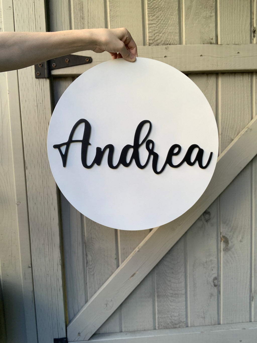 White 3D round wooden name sign with black cursive letters spelling Andrea held by hand outdoors