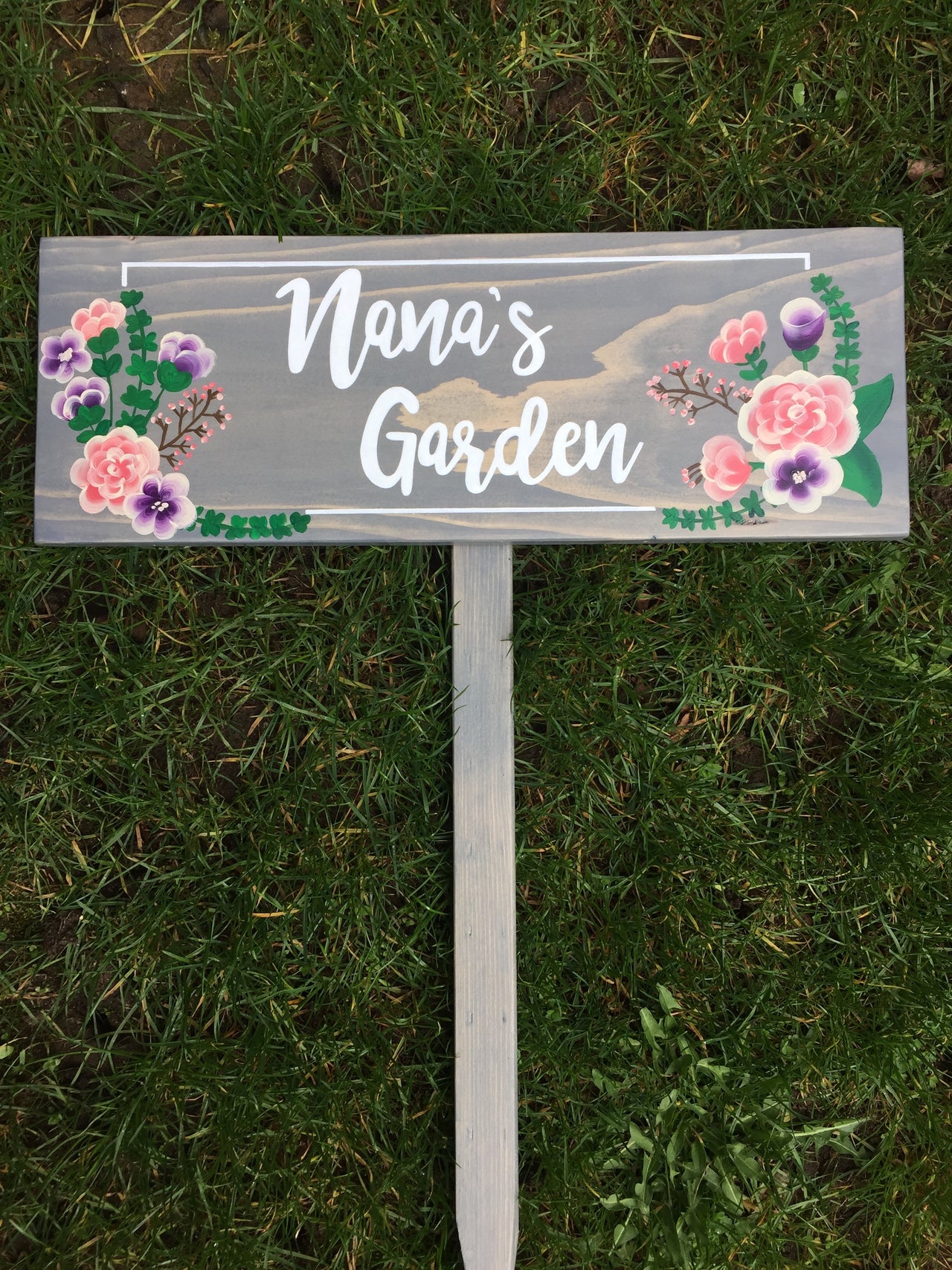 Large personalized wooden garden sign with white cursive letters and pink and purple floral accents on gray stained wood background