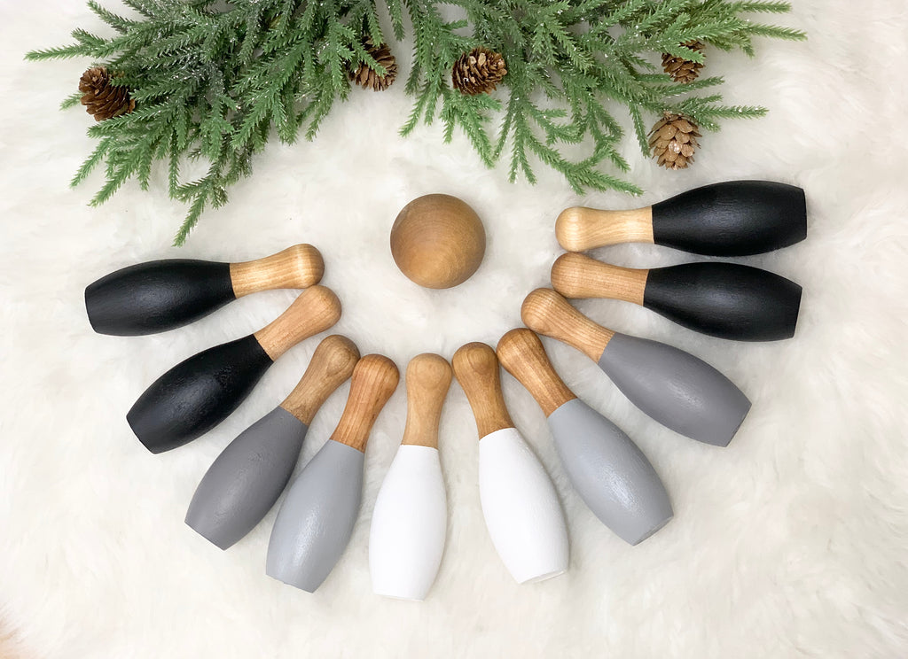 Monochrome wood bowling set with 10 pieces arranged on white fur background with green pine and pinecones above