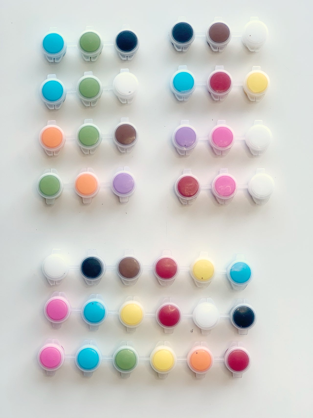 Small round paint pots in various pastel and bright colors arranged in neat rows on white background