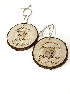 Two round wooden "Baby's First Christmas" ornaments with bark edges and rustic twine on white background
