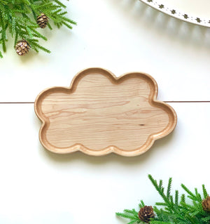 Natural wooden cloud-shaped sensory tray with smooth finish on white surface surrounded by green pine branches with cones