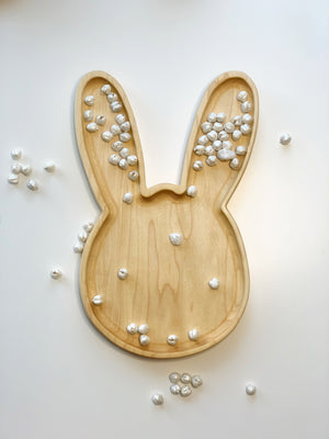 Large natural wooden bunny-shaped sensory tray with small white textured balls scattered inside and around on white background