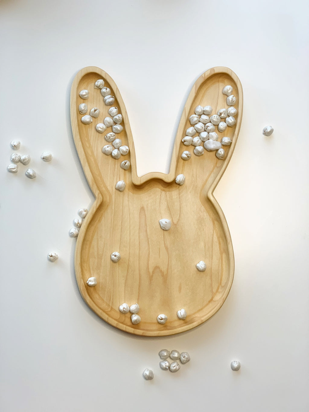 Large natural wooden bunny-shaped sensory tray with small white textured balls scattered inside and around on white background
