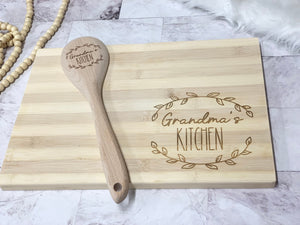 Personalized wooden spoon and cutting board set engraved with "Grandma's Kitchen" and decorative leaf design on light wood background