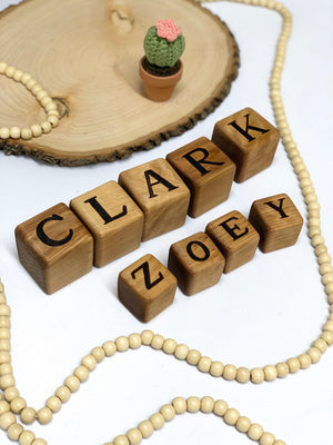 Custom 2-inch wooden blocks with engraved letters arranged to form names on a white surface with decorative items.