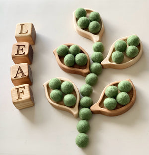 Small wooden leaf-shaped trays with green felt balls and wooden letter blocks spelling leaf on white surface