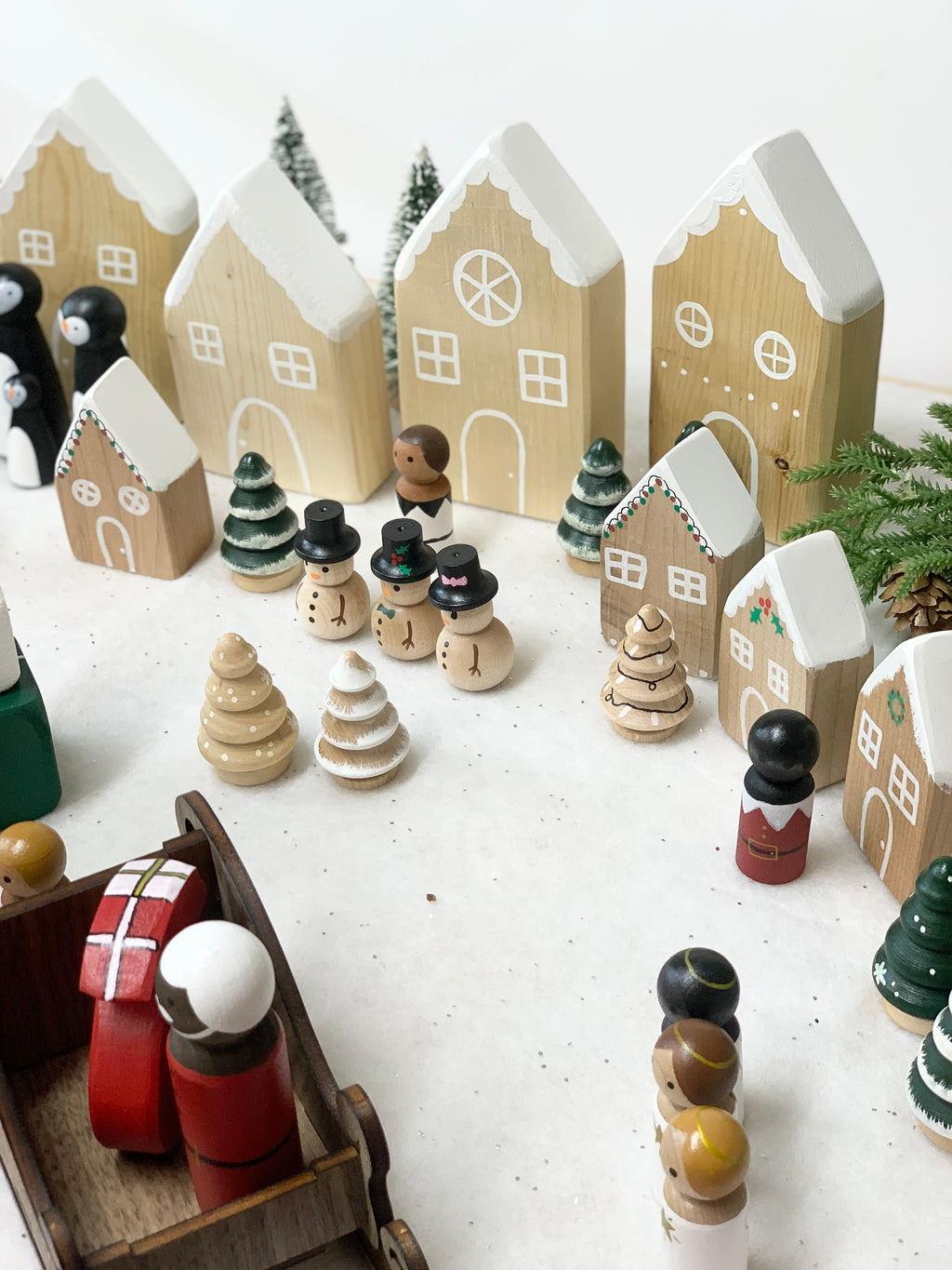 Hand-painted wooden Christmas peg dolls and miniature houses with snowy roofs and decorated trees on white surface