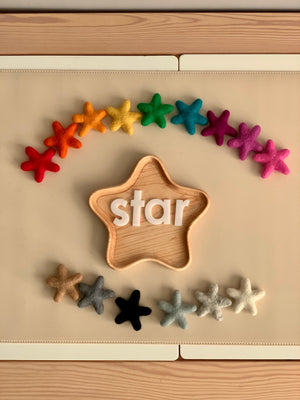 Handmade wool felt stars in various colors arranged around a wooden star-shaped tray with white letter blocks spelling star
