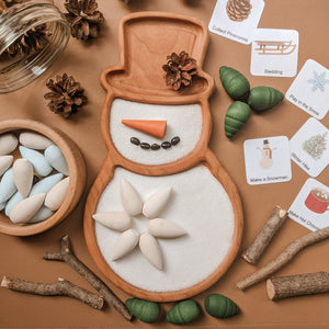 Snow person sensory tray with wooden carrot nose, coffee bean smile, and white wooden pieces on brown background with nature elements
