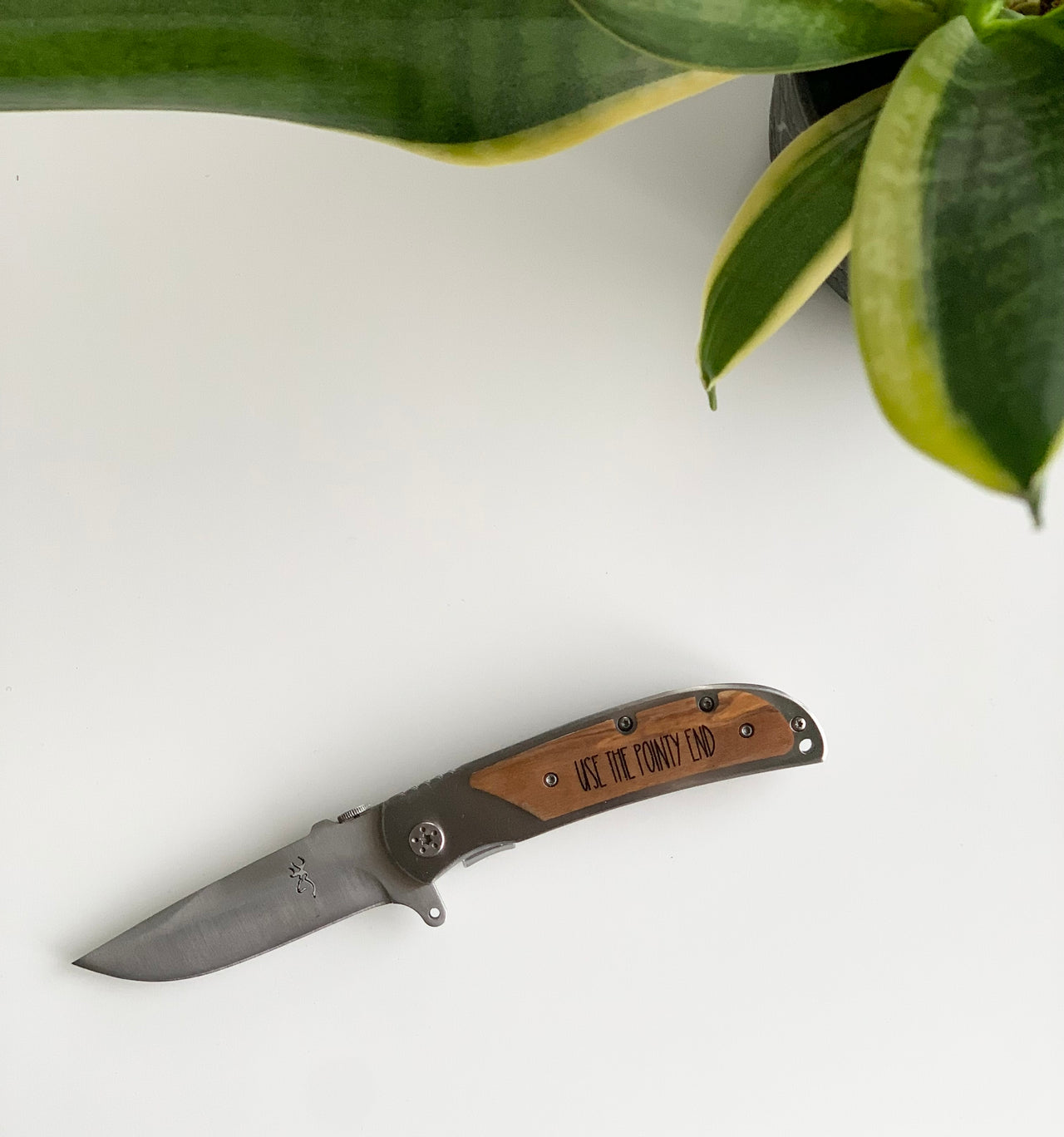 Custom wooden pocket knife with stainless steel blade and engraved personalized handle on white background with plant leaves