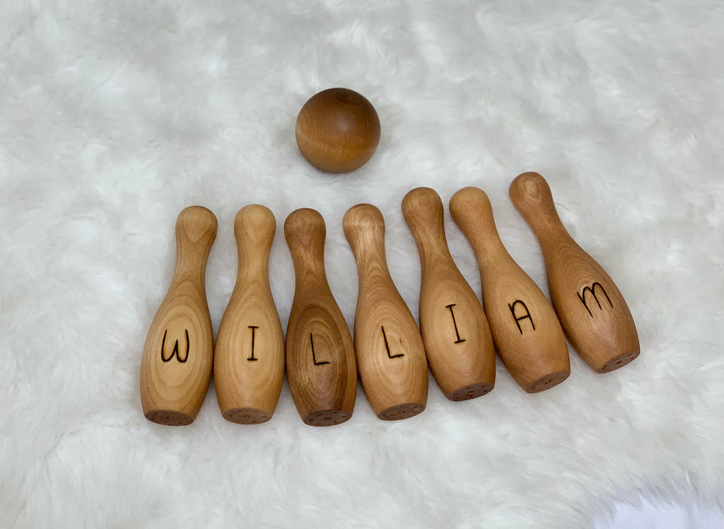 Personalized wooden bowling pins spelling William with a wooden ball on a white fuzzy background
