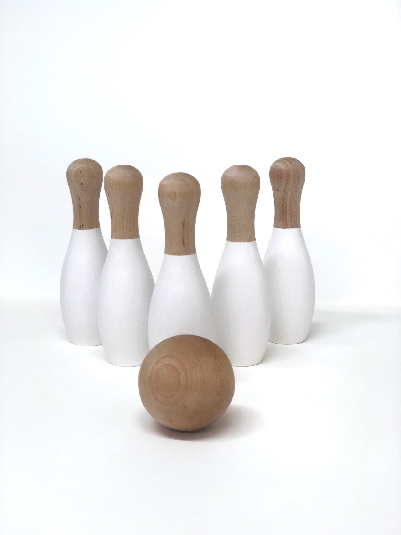 Natural wooden 5-pin bowling set with white painted bodies and smooth round wooden ball on white background