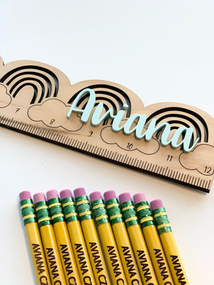 Natural wooden personalized rainbow ruler with light blue cursive name and black measurement markings on white background
