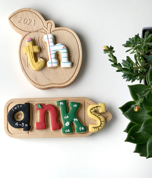 Personalized wooden teacher name plate with colorful letters and educational designs on apple and rectangular plaques with plants nearby
