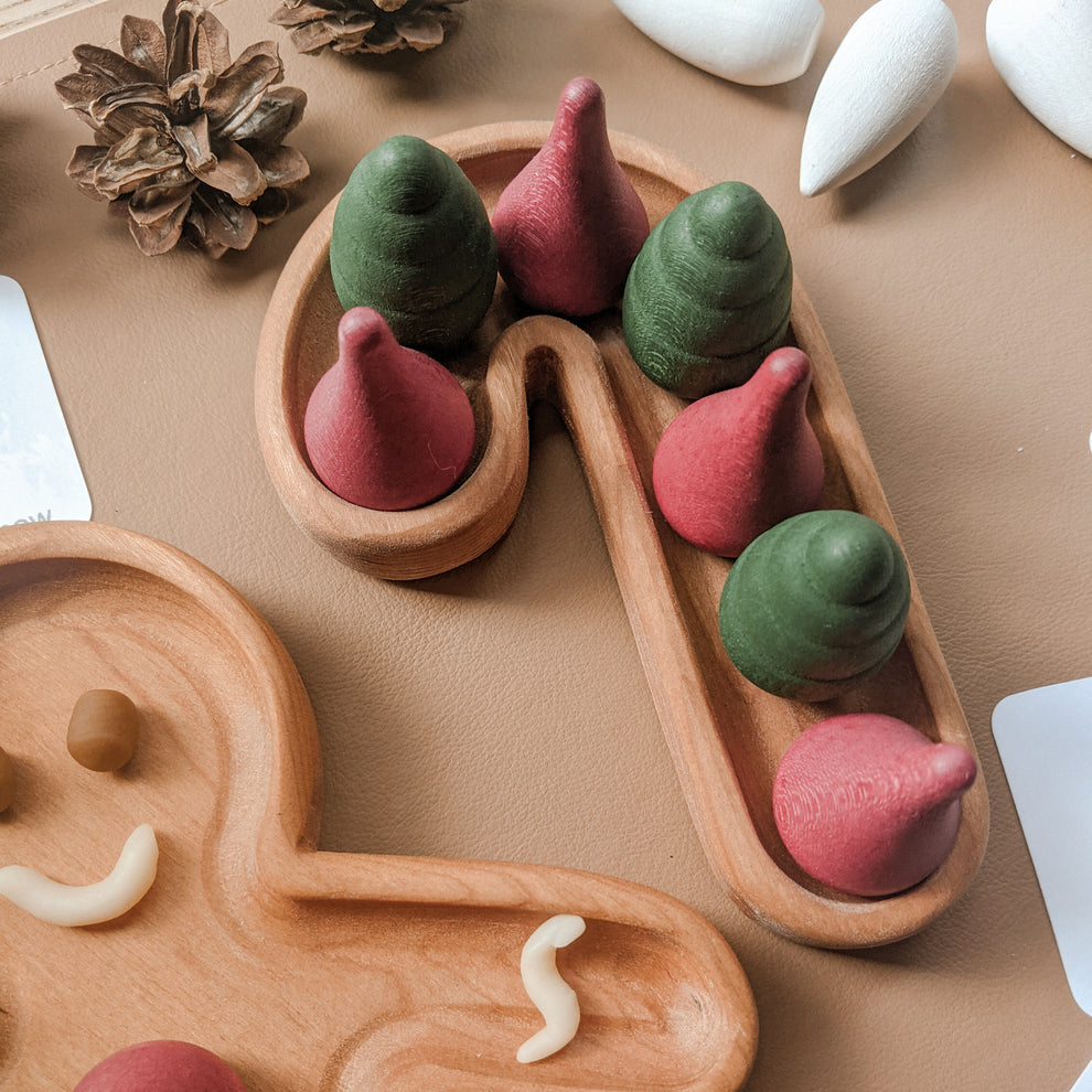 Natural wooden candy cane shaped sensory tray with red and green wooden cone pieces on tan background