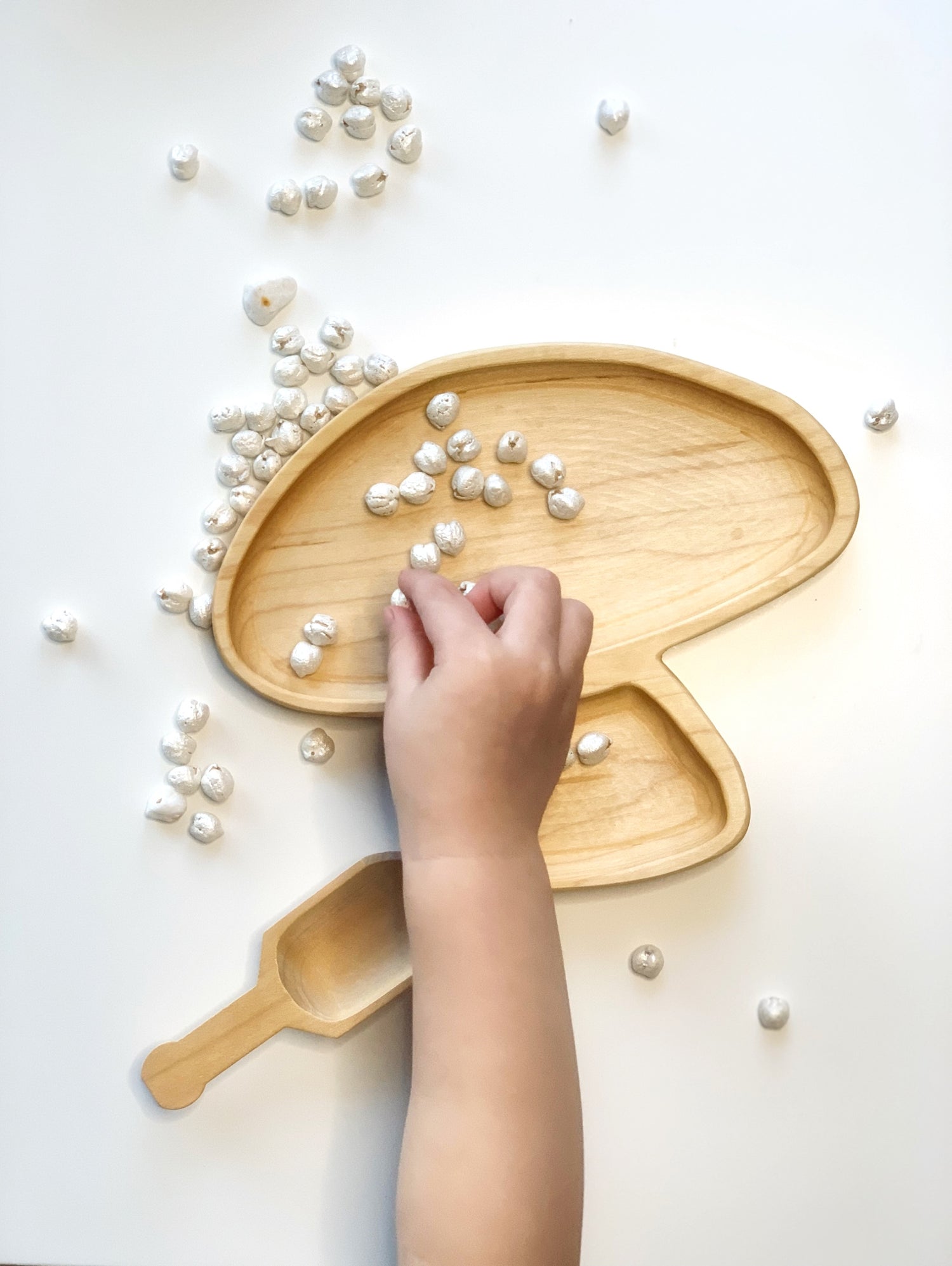 Natural wooden mushroom-shaped plate with a small scoop and scattered white sensory beads on white background