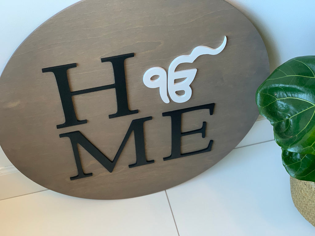 Oval wooden 3D round name sign with black letters and white decorative symbol on natural wood background near green plant