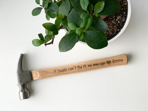 Personalized wooden hammer with laser engraved custom message and heart icon on natural wood handle near green potted plant