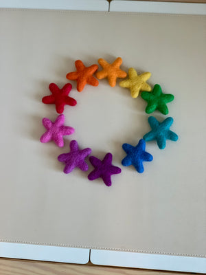 Handmade rainbow felt stars in various colors arranged in a circle on a light beige surface