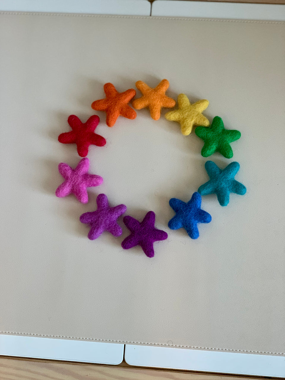 Handmade rainbow felt stars in various colors arranged in a circle on a light beige surface