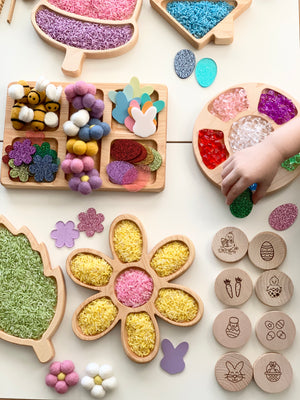 Wooden Easter memory game pieces with engraved holiday icons arranged near colorful textured craft materials in wooden trays