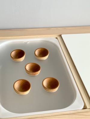 Set of five small wooden bowls inside a white acrylic tray on a light natural wood frame surface