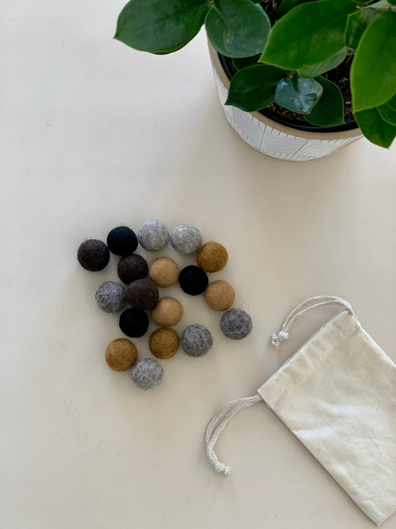 Assortment of 18 small felt balls in soil and rock colors with natural drawstring bag and green potted plant on white surface