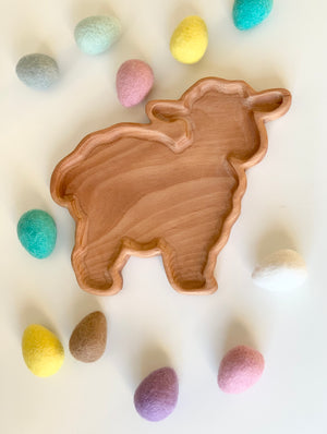 Wooden lamb-shaped sensory tray surrounded by pastel felt eggs on white surface for spring activities