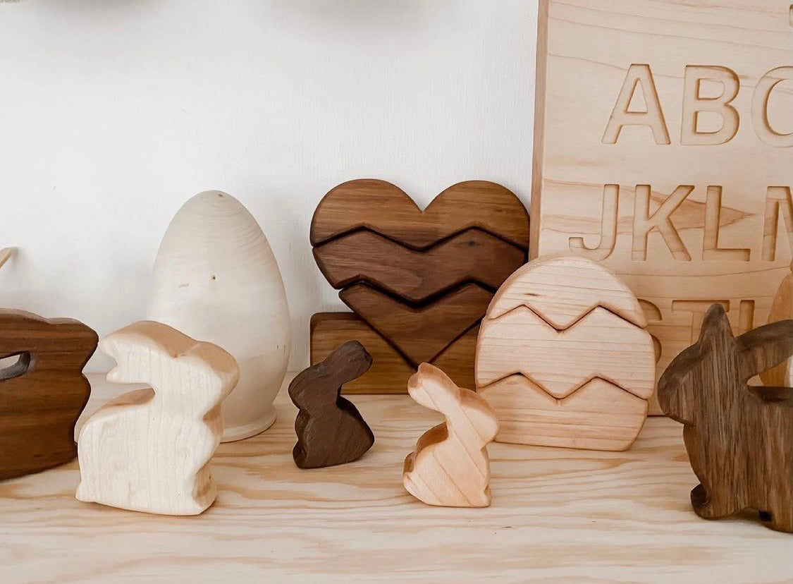 Natural wooden heart stacking toy with zigzag patterns and assorted wooden bunny figures on light wood surface