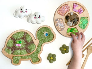Natural wooden turtle sensory tray filled with colored rice and a round tray with compartments holding gems and stones on white background
